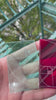 Hand holding two laser-engraved acrylic cards by PIT//STOP—one transparent and one red—etched with a golden ratio Fibonacci spiral, showcasing custom acrylic merchandise and precision engraving.