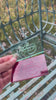 Hand holding two laser-engraved acrylic cards—one mint/ transparent and one red—displaying the PIT//STOP logo, demonstrating custom etched branding and merchandise prototypes, against a blurred outdoor background