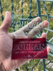 Close-up of a hand holding two engraved acrylic campaign-style cards—one red and one clear—featuring the PIT//STOP endorsement design for Zohran for New York City, showcasing etched typography and transparent material. Text says "PIT//STOP ENDORSES ZOHRAN FOR NEW YORK CITY"